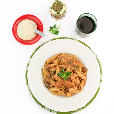 Penne pasta with vodka sauce on a white plate with a glass of red wine.
