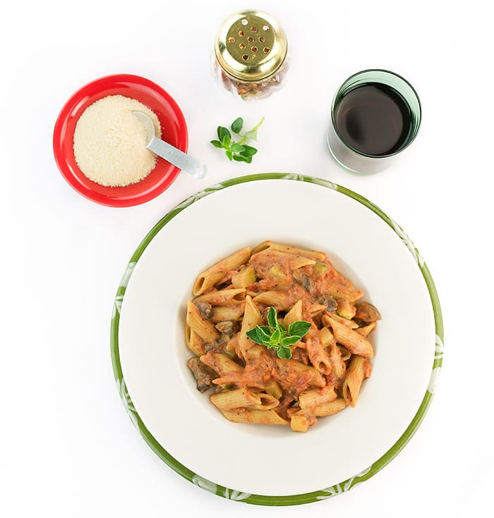Penne pasta with vodka sauce on a white plate with a glass of red wine.