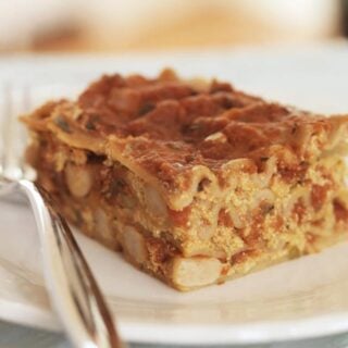 A slice of vegan lasagna on a white plate with a silver fork.