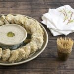 Panko crusted pickles in a circle around vegan ranch dressing on a wooden background.