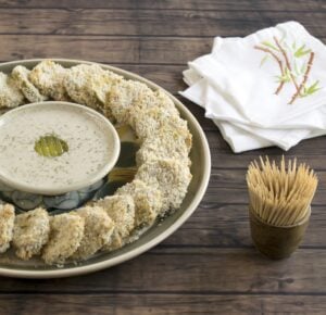 Panko crusted pickles in a circle around vegan ranch dressing on a wooden background.