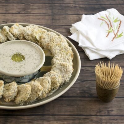 Panko crusted pickles in a circle around vegan ranch dressing on a wooden background.