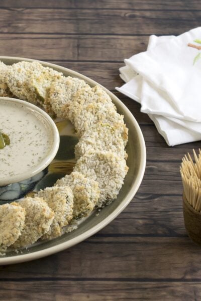 Panko crusted pickles in a circle around vegan ranch dressing on a wooden background.