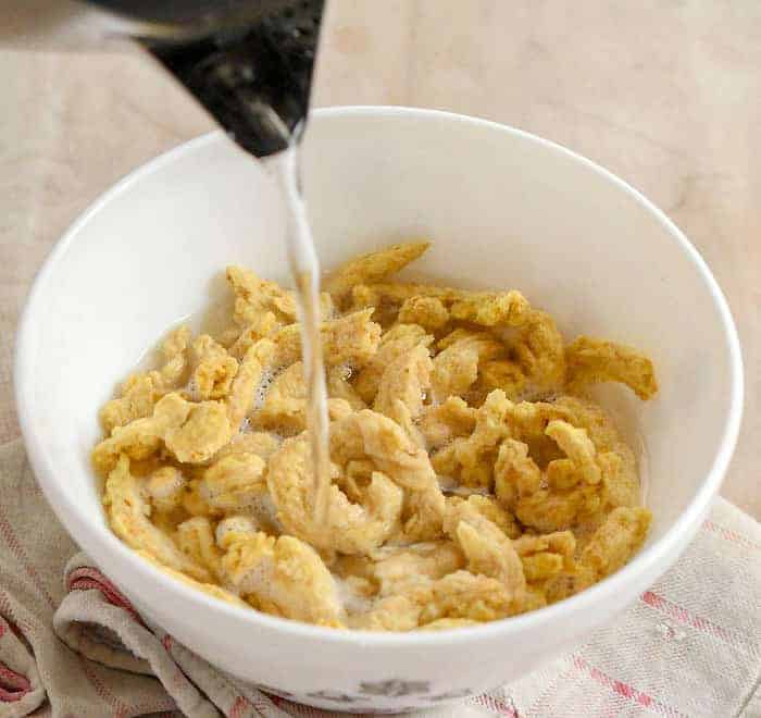 Hot water being poureed over soy curls in white bowl.