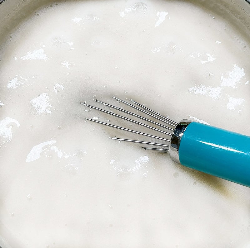 The pudding thickening over the heat with a blue whisk in the pan.