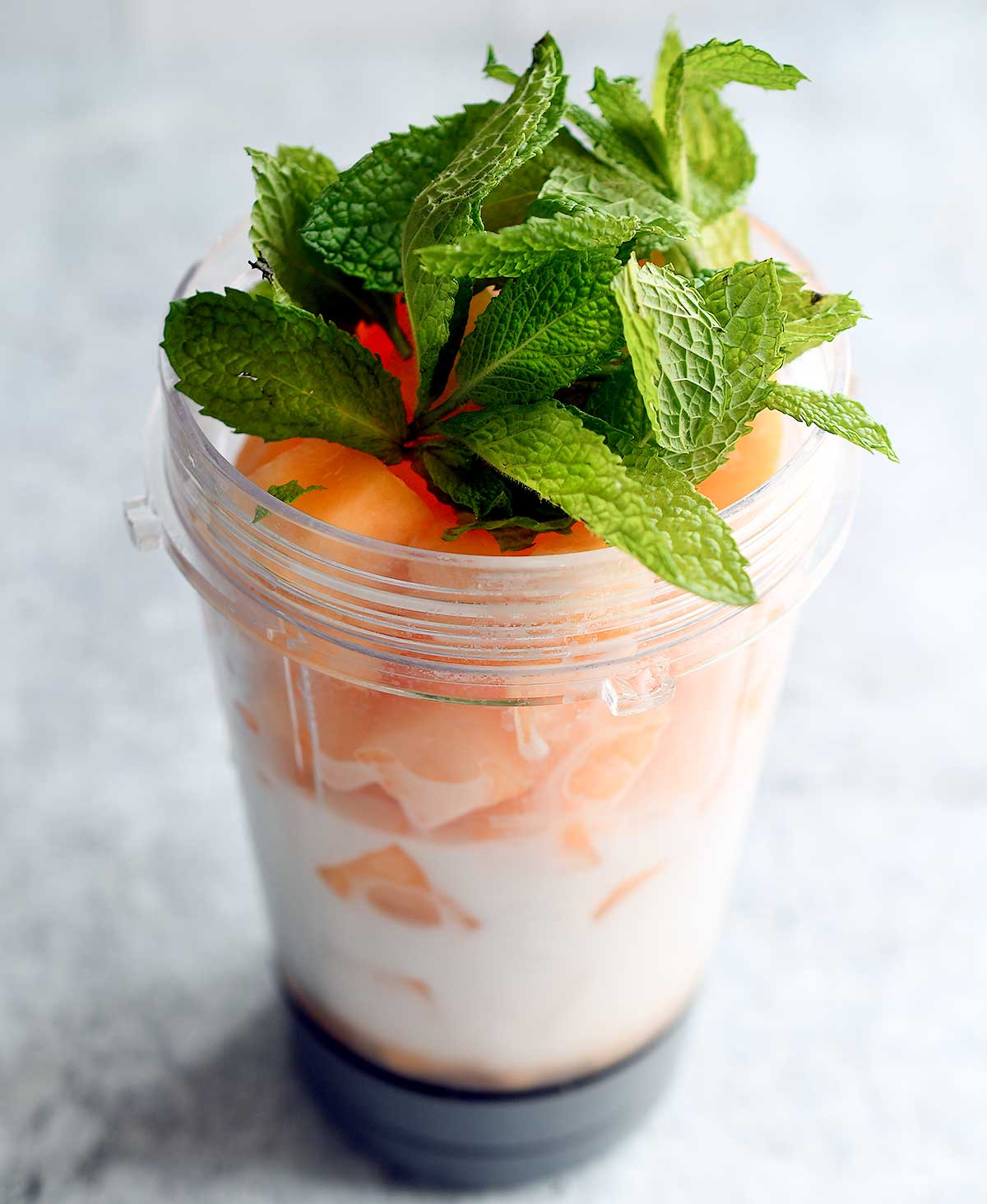 A Ninja Smoothie blender container with almond milk, cantaloupe, and fresh mint for a cantaloupe sorbet.