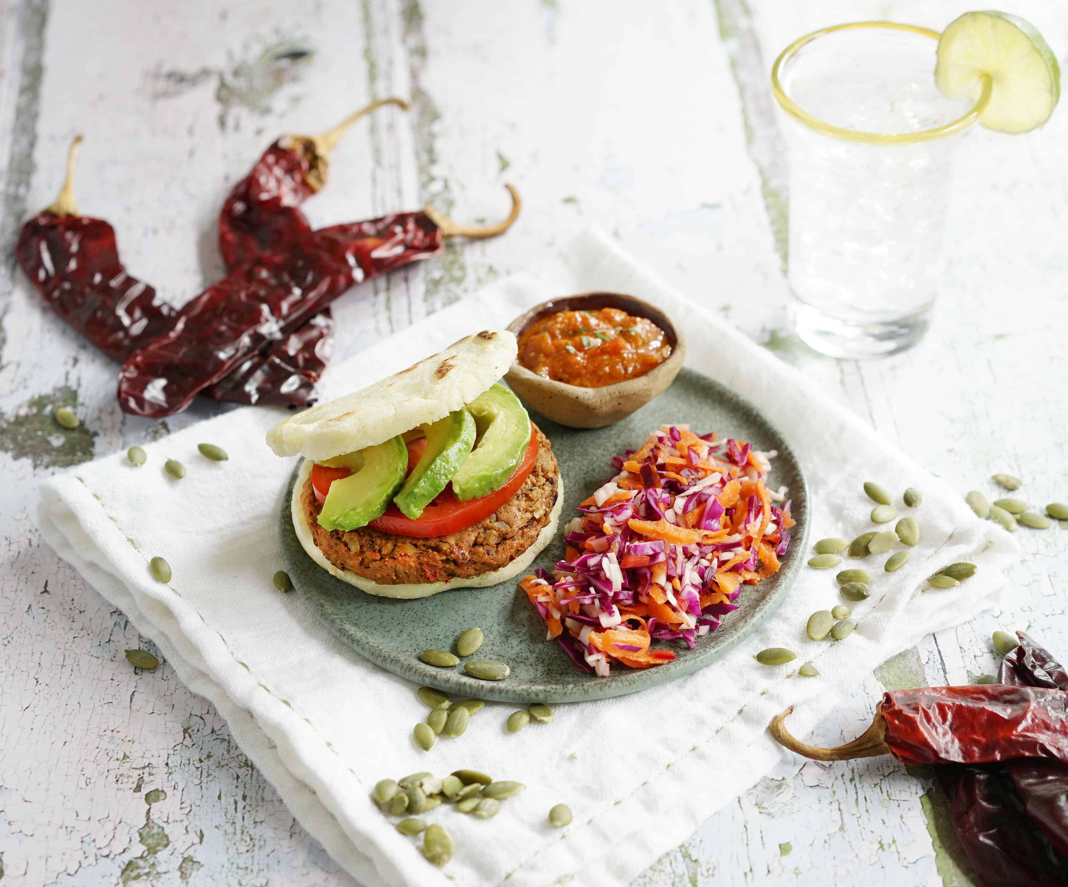 Chile Pepita Idaho® Potato Veggie Burgers in a ceramic plate with dried chilies and pepitas scattered on a table with a glass of iced-water