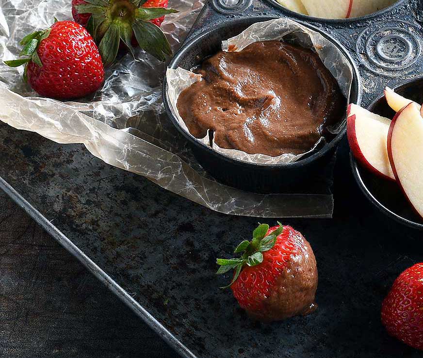 Chocolate hummus in an old muffin tin with slices apples and strawberries.
