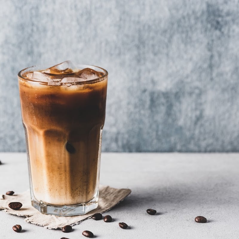 Iced cold brew coffee in a glass cup with almond milk surround by a scattering of coffee beans