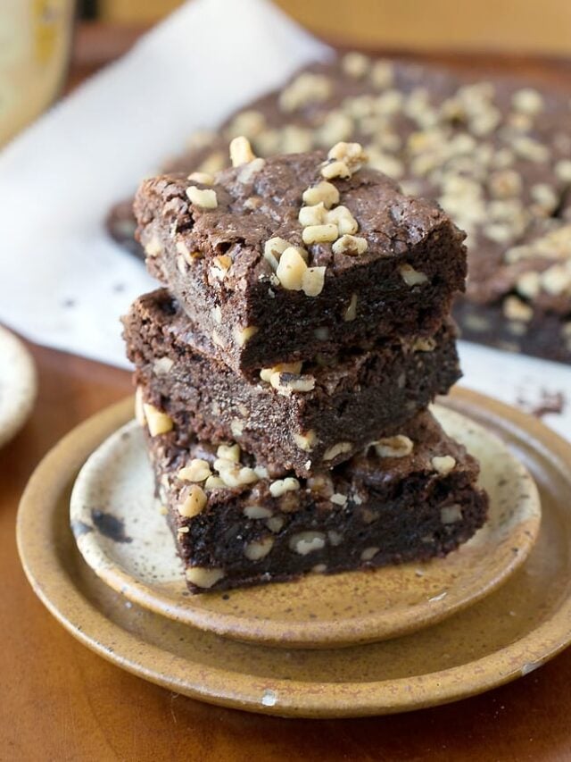 Brownies made with teff flour piles up on top of brown pottery plates.