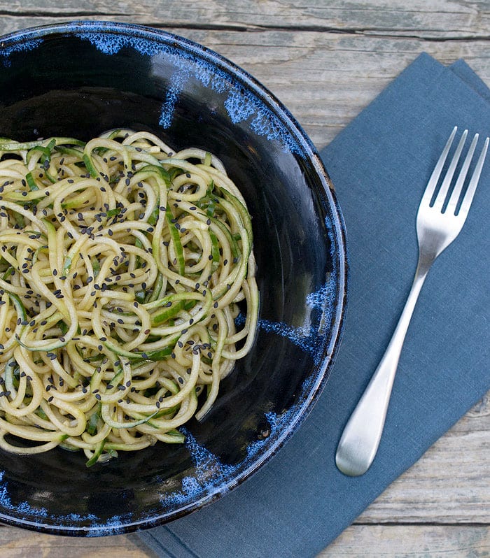 Cucumber noodles with sesame seeds in a black bowl with fork on the side