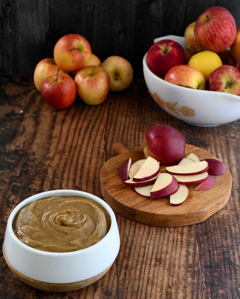 Date caramel vegan hummus swirled in a white bowl on a dark wooden tables top with apples and sliced red apples.