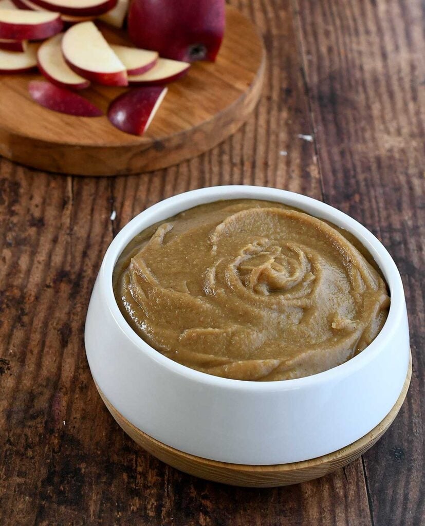 Date caramel vegan hummus swirled in a white bowl on a dark wooden table.