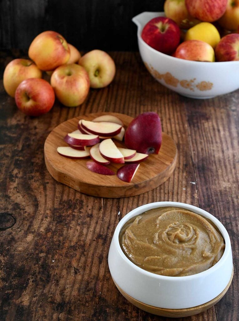 Date caramel vegan hummus swirled in a white bowl on a dark wooden tables top with apples and sliced red apples.
