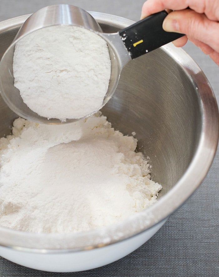A half-filled measuring cup adding into a stainless mixing bowl with cornstarch