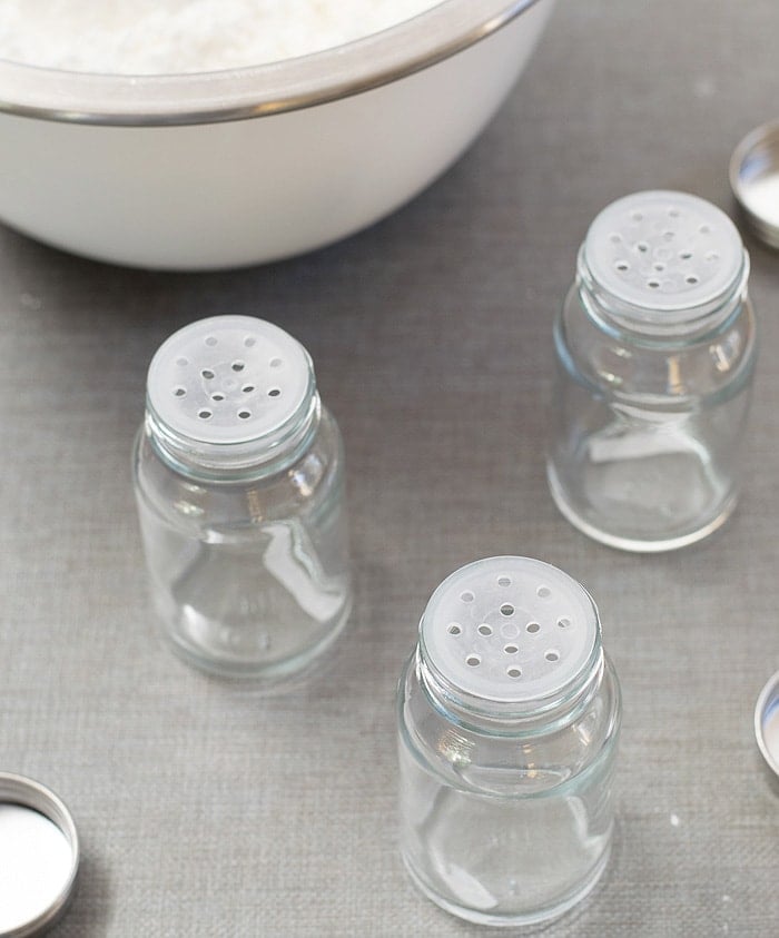 Three empty glass bottle jars placed on a light grayish table near the stainless mixing bowl