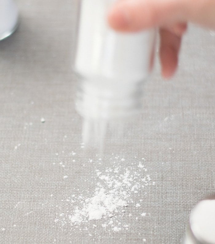 A hand pouring the DIY Body Powder on a grayish linen