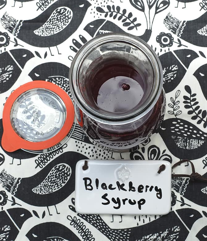 DIY Fresh Blackberry Syrup Blackberry Syrup in a weck carafe on a graphic bird tablecloth