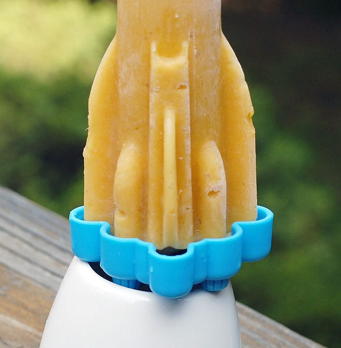 Vegan Mango Lassi Popsicles on my Tovolo rocket pop mold placed on a ceramic base sitting on a wooden table