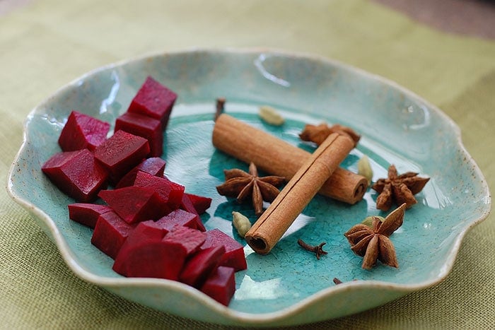 Blue pottery plate of cut beets, cinnamon sticks, cardamom pods, and star anise