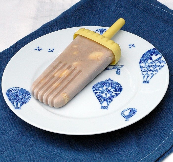vegan banana pudding popsicle on a white-and-blue plate placed on top of a blue cloth and another white cloth, top-side view
