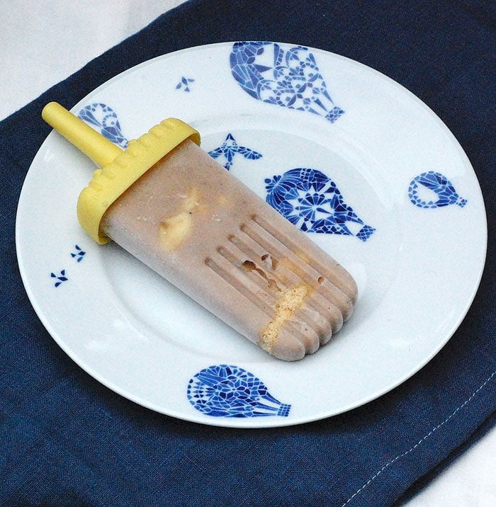 vegan banana pudding popsicle on a white-and-blue plate placed on top of a blue cloth and another white cloth