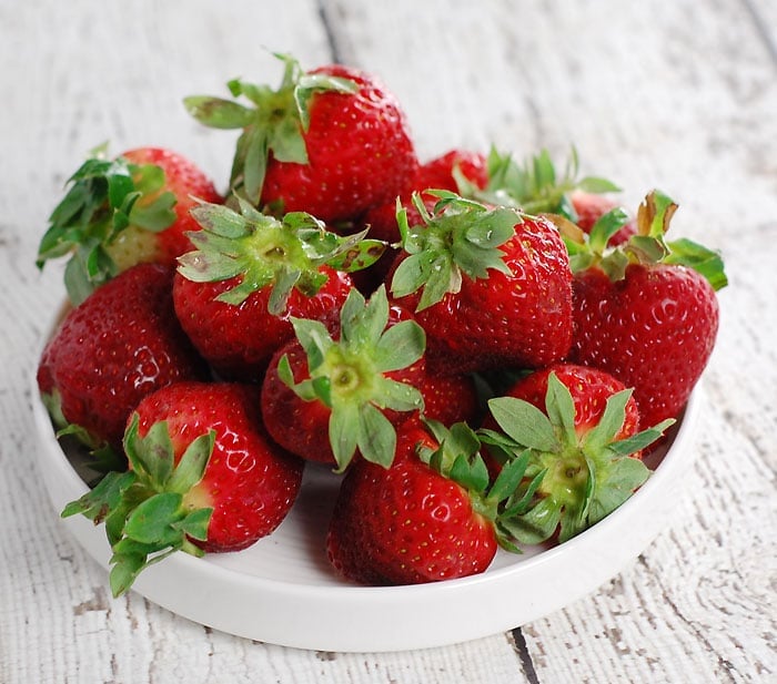 a small white plate filled with strawberries, sitting on a wooden table painted in white