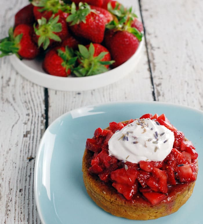 Lavender Gin Strawberry Shortcake made with Aquafaba sitting on a pale blue plate and on top of a wooden table painted in white; with a plate full of strawberries in the background