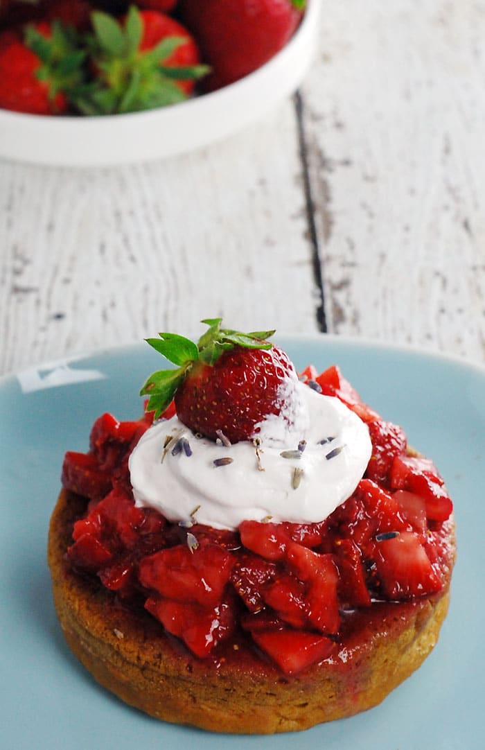 Lavender Gin Strawberry Shortcake made with Aquafaba sitting on a pale blue plate and on top of a wooden table painted in white; with a plate full of strawberries in the background