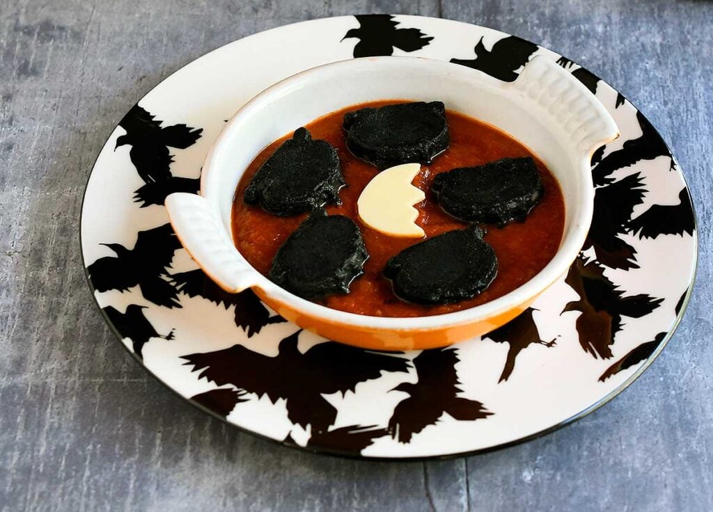 Cauldron black gnocchi in a small orange casserole dish on a raven plate.