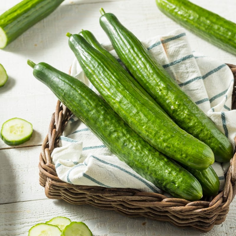 English cucumbers on top of a white and blue-striped cloth inside a basket