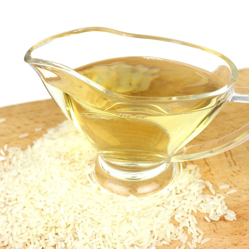 rice vinegar in a glass cup with white rice grains surrounding it