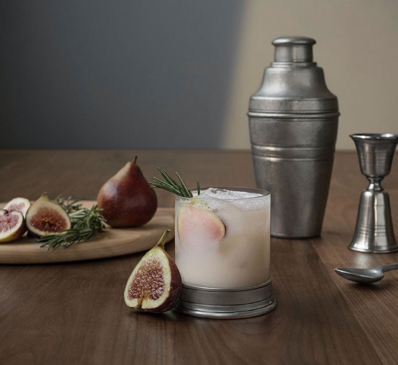 Fig shrub cocktail in a glass with a slice of fresh fig and a sprig of rosemary.
