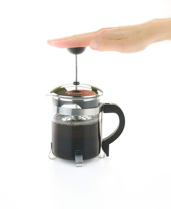 Hand pressing down the plunger on a French press full of coffee