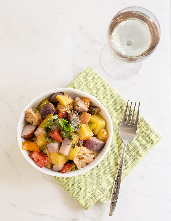Instant Pot Potato Panzanella Salad in white bowl on lime napkin with a glass of wine.