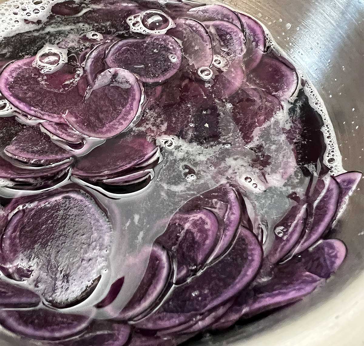 Purple potato slices in a bowl of water.