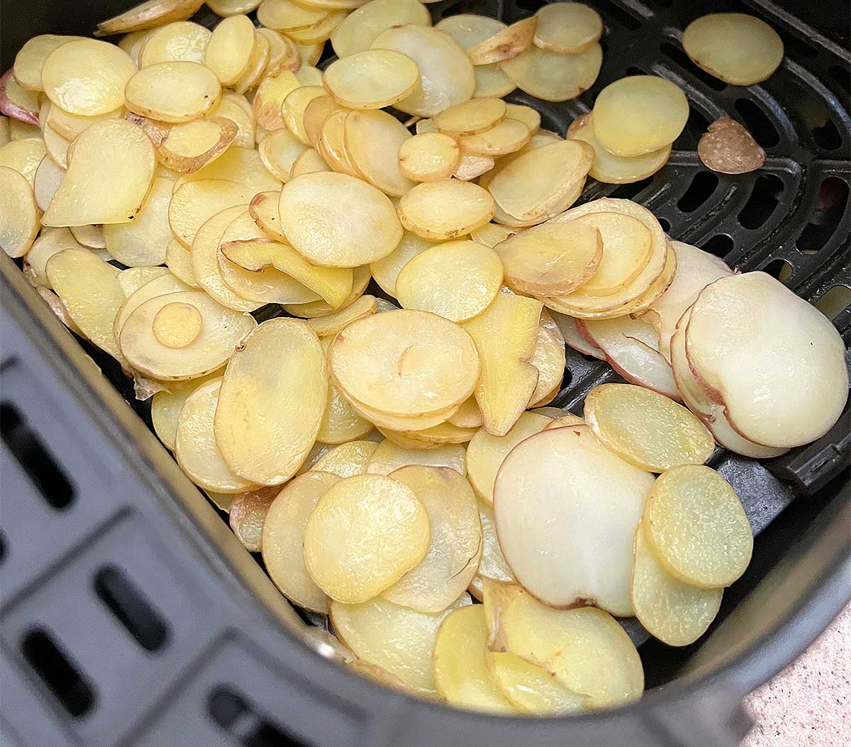 Sliced yellow potatoes in an air fryer basket.