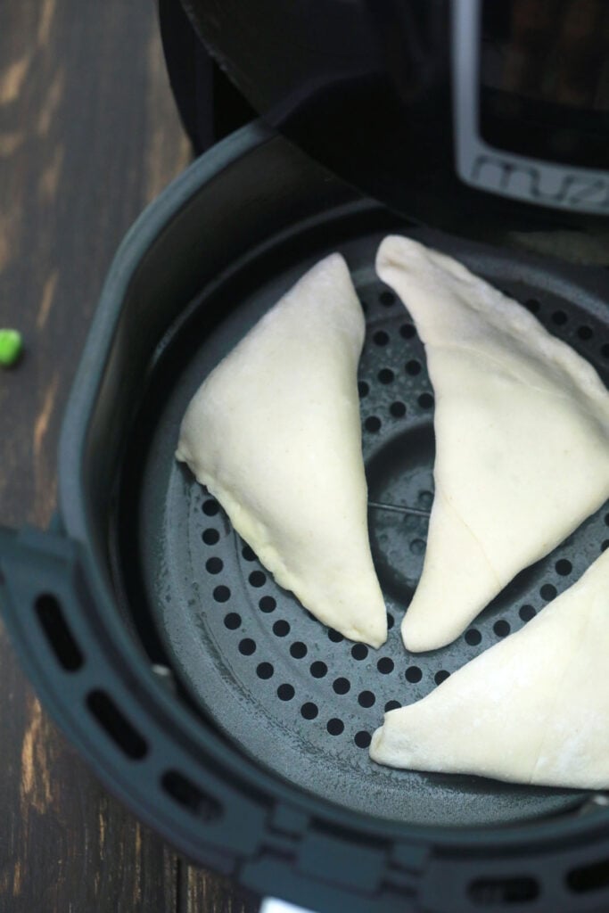 3 uncooked vegan samosas in the air fryer basket.