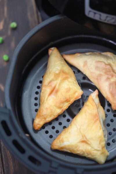 3 vegan samosas in the air fryer basket after frying to golden perfection.