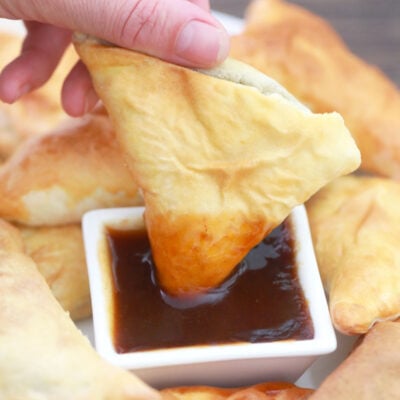 hand dipping an air-fried vegan samosa in tamarind chutney.