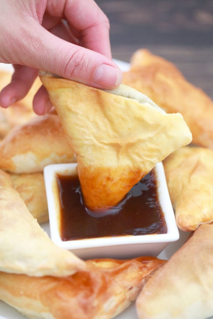 hand dipping an air-fried vegan samosa in tamarind chutney.