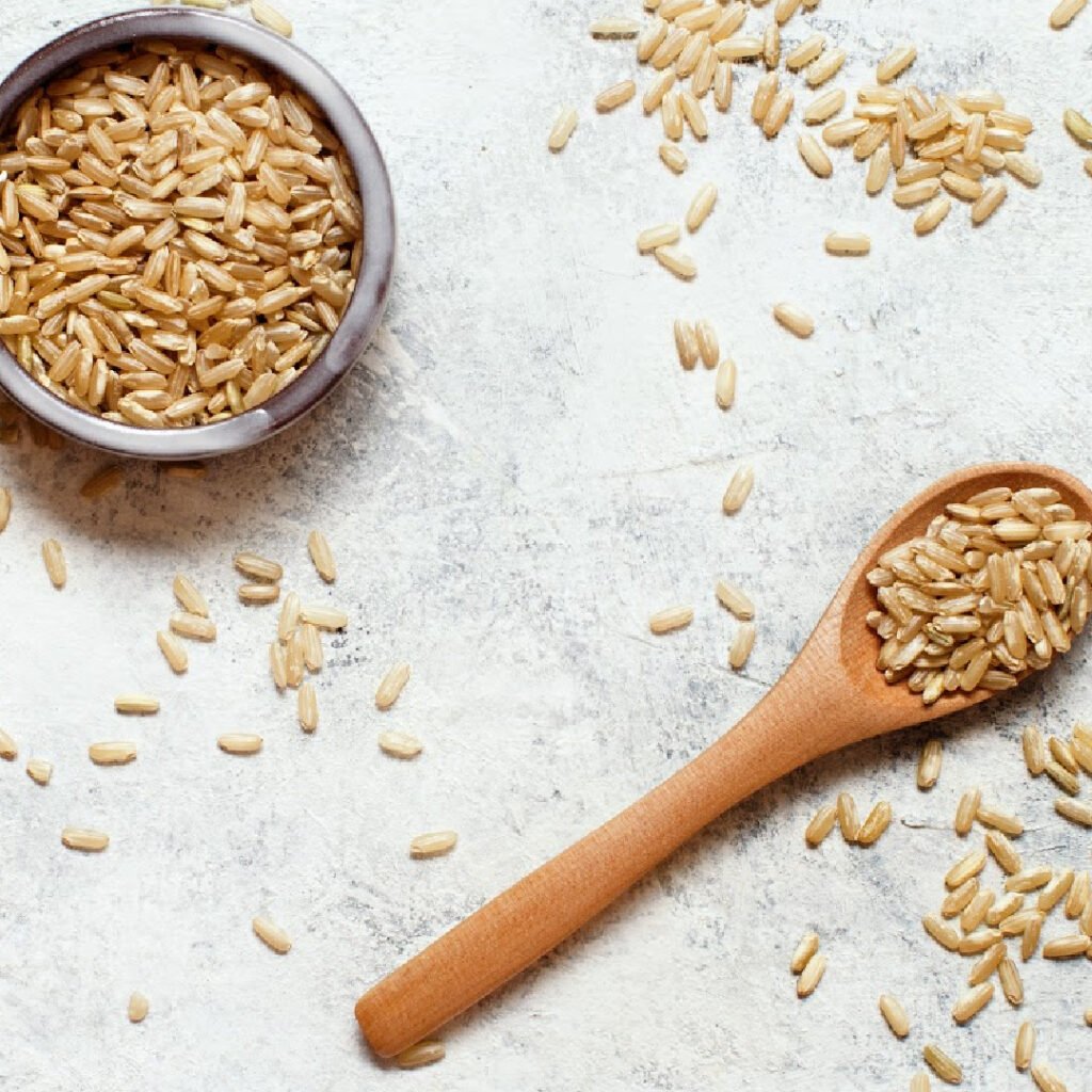 Brown rice in a wooden bowl with a spoon top view.