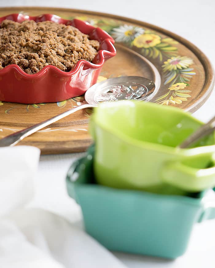 Vegan Air Fryer Blueberry Apple Crumble in a red ruffled baking dish on a wooden plate with painted flowers.