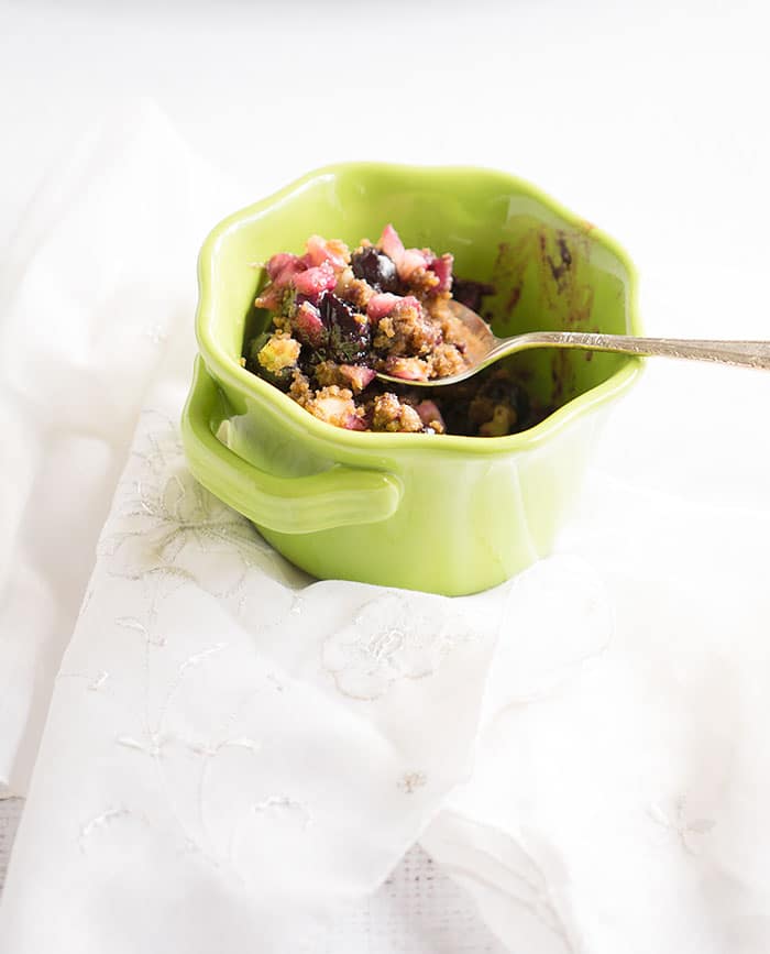 A single serving of apple blueberry crumble in a green bowl with handles.