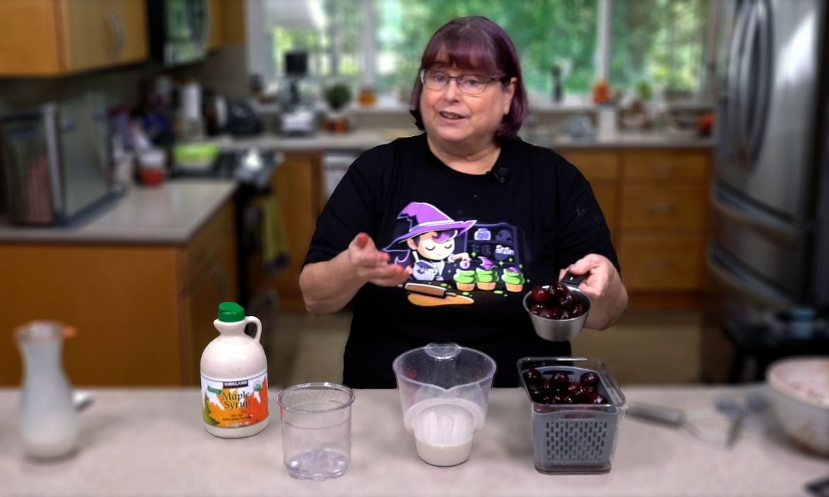 Kathy in front of an OXO measuting cup of homemade nondairy milk, maples syrup, and cherries