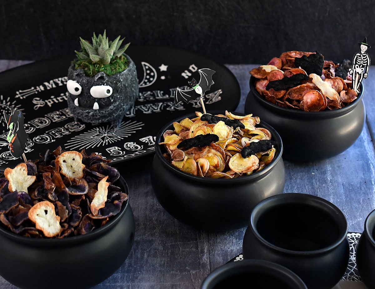 Colored potato chips in black cauldron bowls set up for a Halloween party