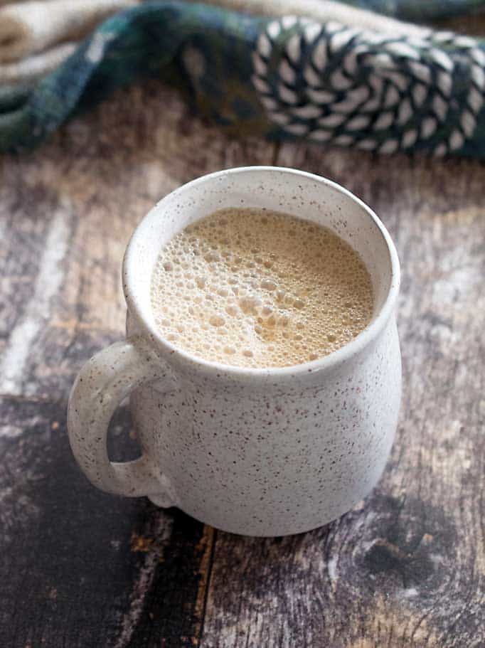 Slow Cooker vegan maple pumpkin latte in a white speckled mug with an artistic scarf on a wood surface