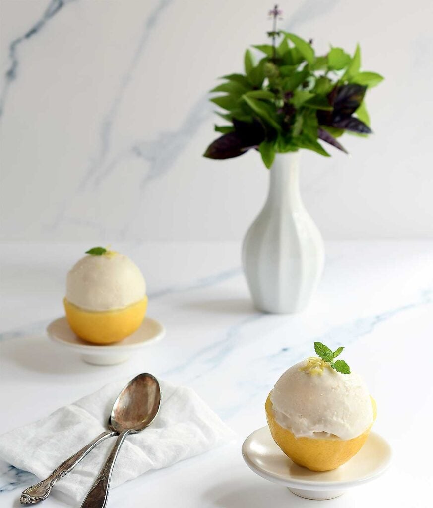Vegan lemon yogurt in lemon cups with lemon basil in the backgrouns.