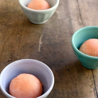 Scoops of watermelon sorbet in small cups on a wooden table.