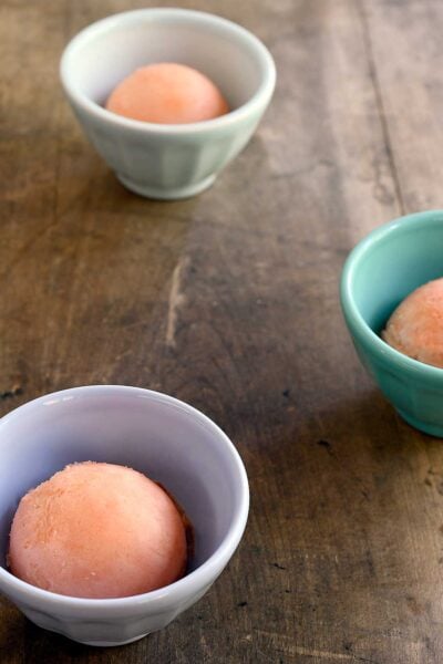 Scoops of watermelon sorbet in small cups on a wooden table.